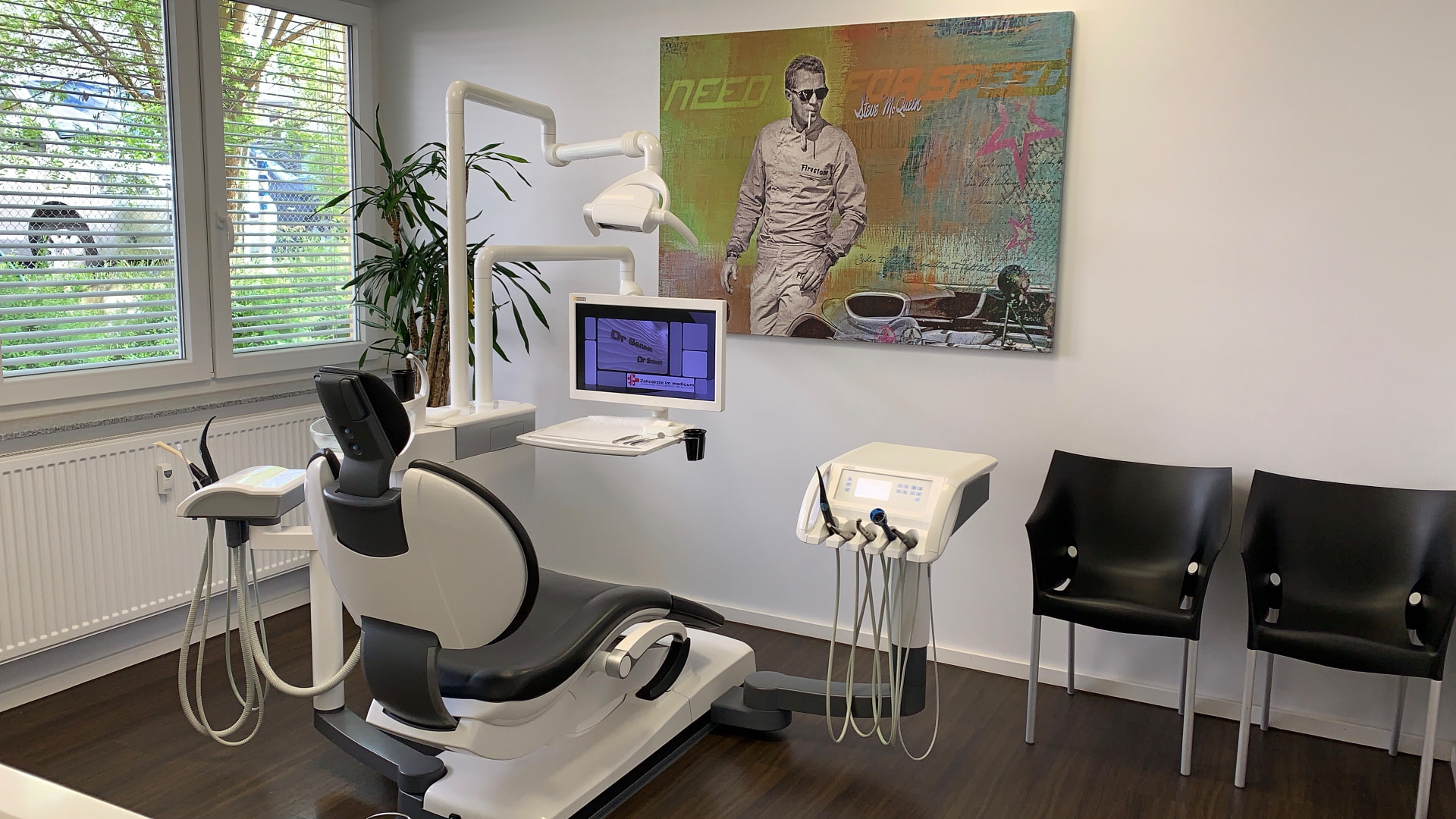 Behandlungszimmer mit Behandlungsstuhl, Monitor und Kunstdruck an der Wand